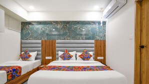 Een hotelkamer met een groot bed, twee kleinere bedden, een marmeren hoofdbord en een houten deur.