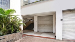 Een modern gebouw met een gesloten garage, een trap naar een hoger gelegen niveau en een kleine tuin met palmbomen.