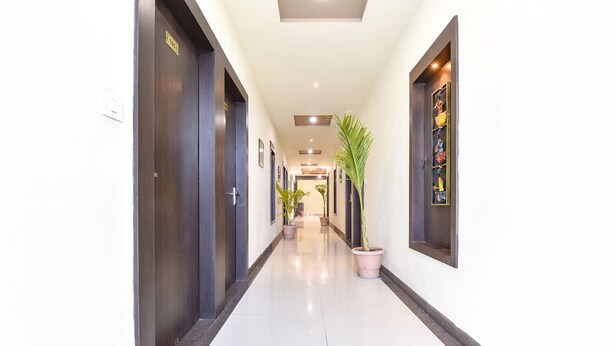 A clean, well-lit hallway with dark doors, potted plants, and a tiled floor. - Fabhotel Golden Palms (Udaipur)