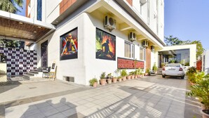 A modern building with large posters on the facade, a tiled entrance area, and potted plants along the walkway. - Fabhotel Golden Palms (Udaipur)