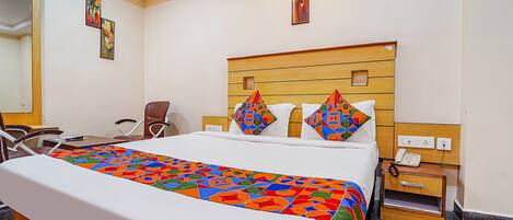 A hotel room with a large bed, a wooden headboard, a bedside table with a phone, and a chair.