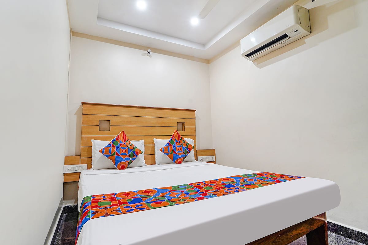 A hotel room with a wooden headboard, a bed with white bedding, two decorative pillows, and a colorful throw blanket.