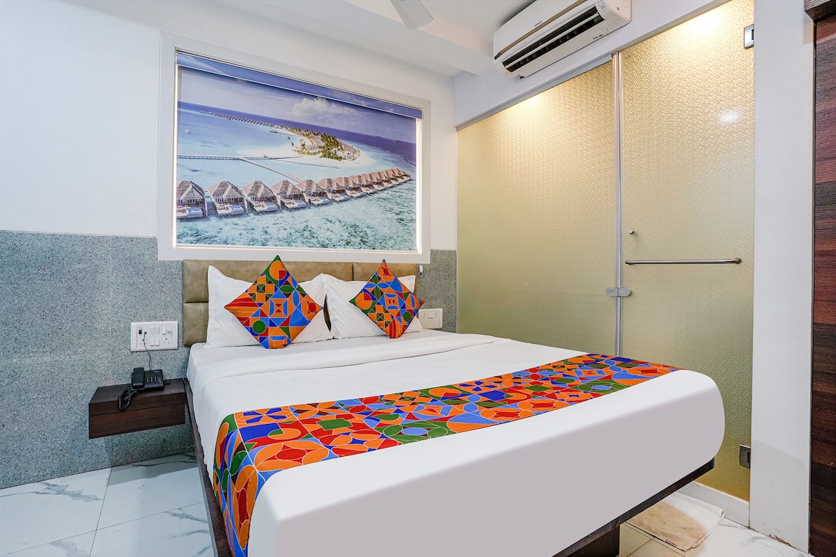 A hotel room with a bed, a nightstand, a phone, a painting of a beach scene, and a shower area.