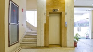 Un hall d’hôtel avec un sol en marbre, une porte de sortie de secours, un escalier et un ascenseur.