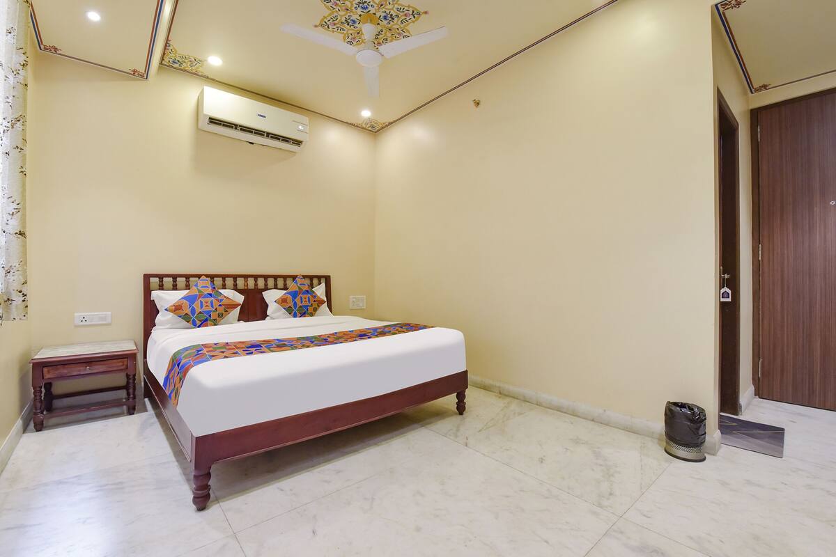 Une chambre à coucher comprenant un lit, une table de chevet, un appareil de climatisation, un ventilateur de plafond et une porte en bois.