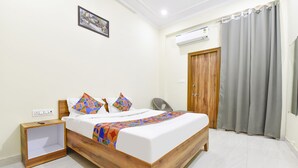 A neatly arranged bedroom with a wooden bed, a bedside table, a chair, and a grey curtain. - Fabhotel Living (Jaipur)