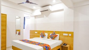 A modern hotel room with a wooden bed frame, a ceiling fan, an air conditioning unit, and a bedside table with a phone. - Fabhotel Saffron Inn I (Pune)