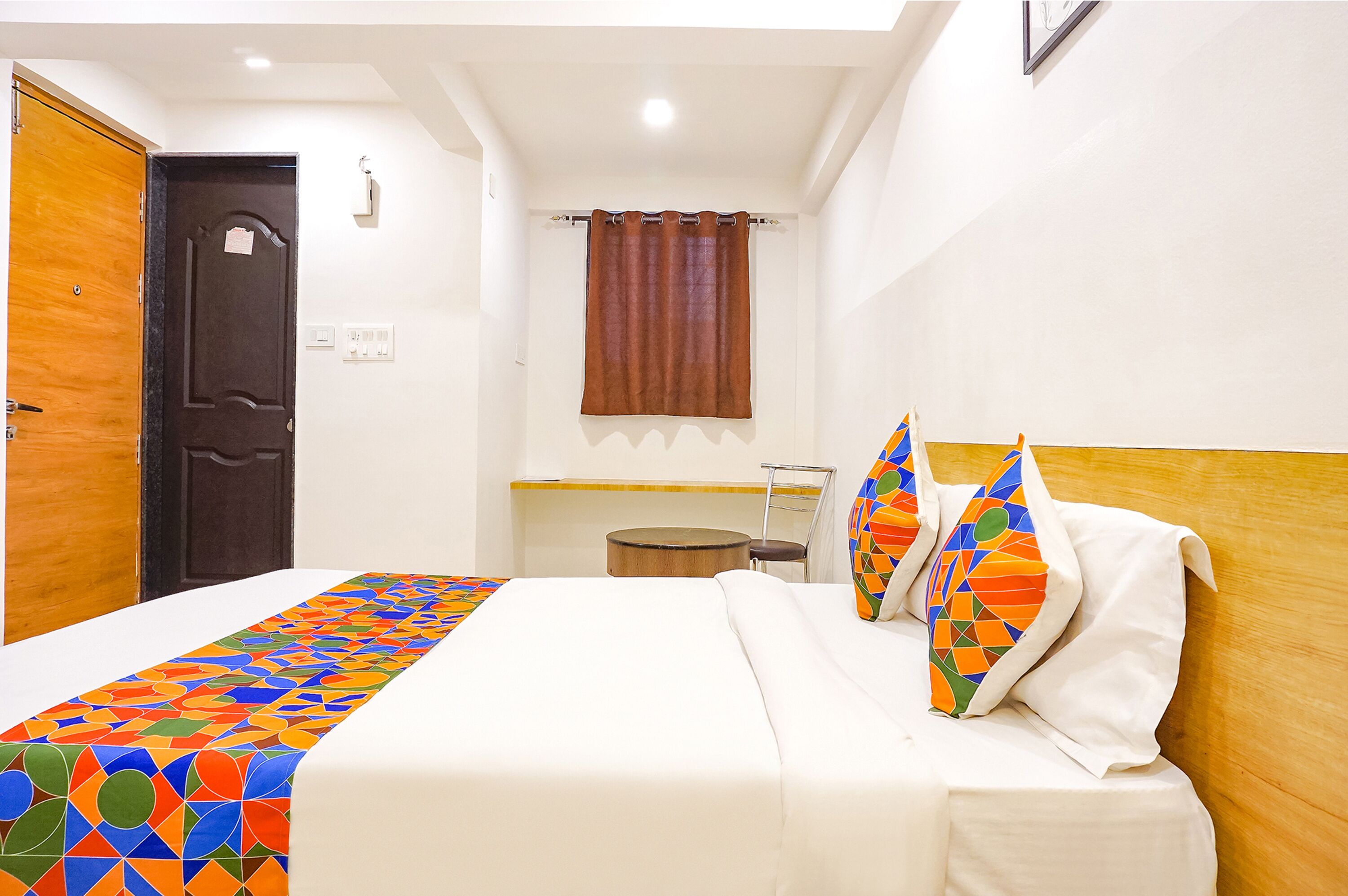 A hotel room with a bed, a wooden door, a small round table, and a window with curtains.