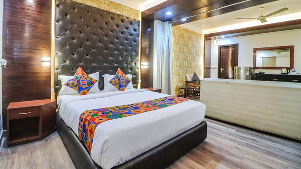A hotel room with a large bed, a tufted headboard, a wooden floor, a nightstand, a desk, and a mirror. - Fabhotel Dwarka Suites (New Delhi)