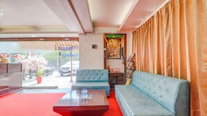A hotel lobby with a red carpet, blue sofas, a wooden coffee table, and a view of parked cars outside. - Fabhotel Dwarka Suites (New Delhi)