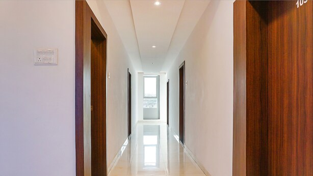 A corridor with wooden doors, a white wall with a power outlet, and a shiny floor. - Fabhotel Spot Light (Sasvad)