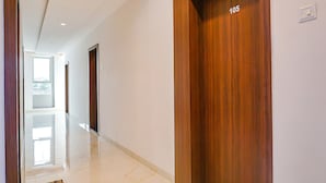 A hallway with a wooden door marked '105', a glossy tiled floor, and a bright interior. - Fabhotel Spot Light (Sasvad)