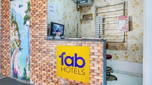 A hotel reception desk with a 'fab hotels' sign, a computer monitor, a calendar, and a floral wallpaper. - Fabhotel Spot Light (Sasvad)