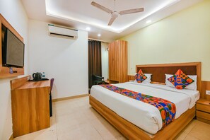 A hotel room with a bed, a desk, a television, and an air conditioning unit.