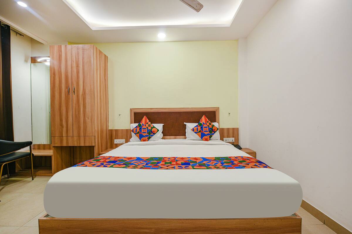 A neatly arranged hotel room with a large bed, a wooden wardrobe, and a chair.