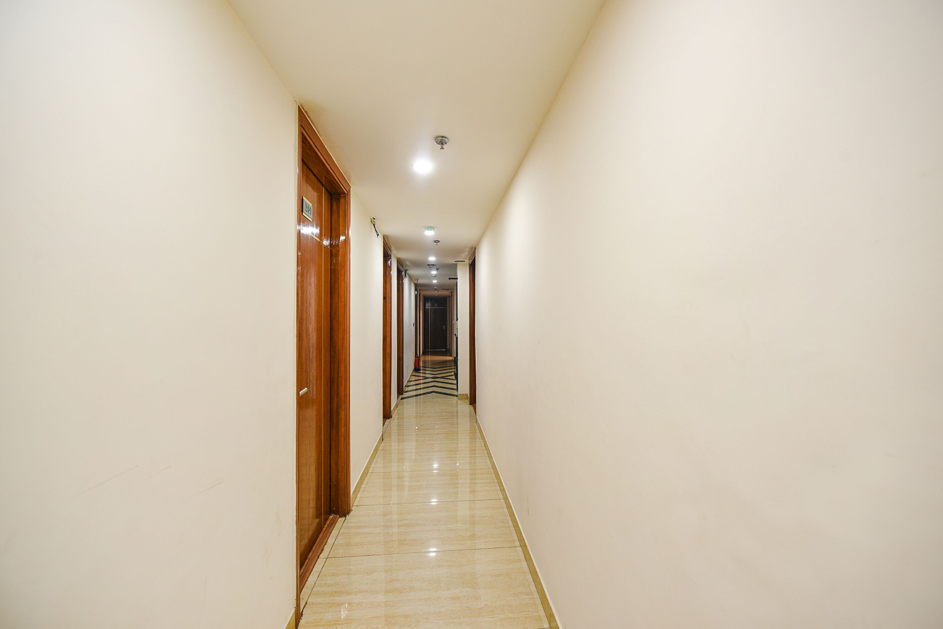 A long, narrow hallway with wooden doors on one side and a tiled floor.
