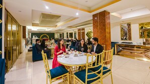 A dining area with round tables and chairs, a decorative wall, and a reception desk. - Fabhotel Prime Blest Park (New Delhi)