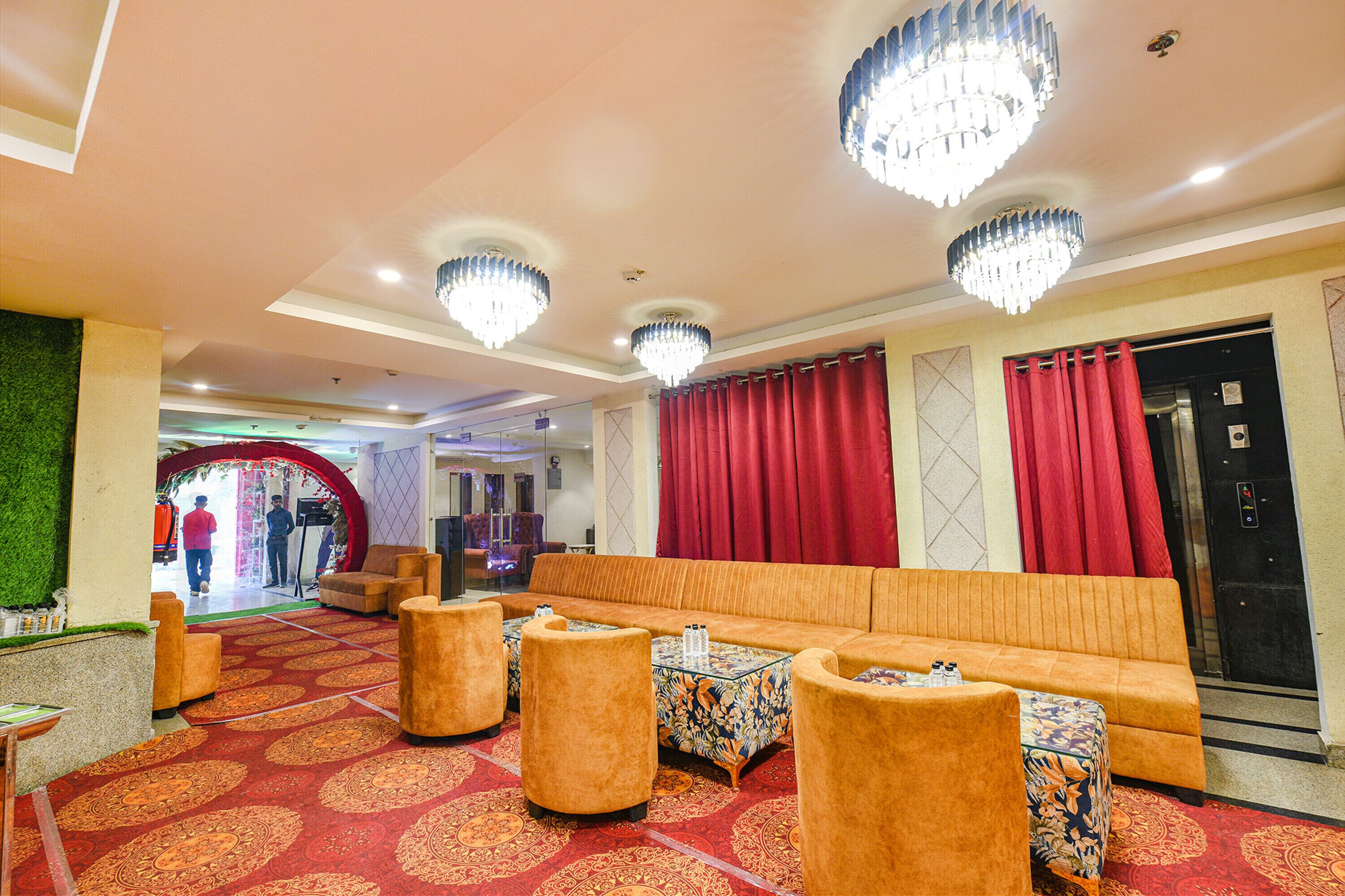 A hotel lobby with a red carpet, a sofa, ottomans, and a chandelier.