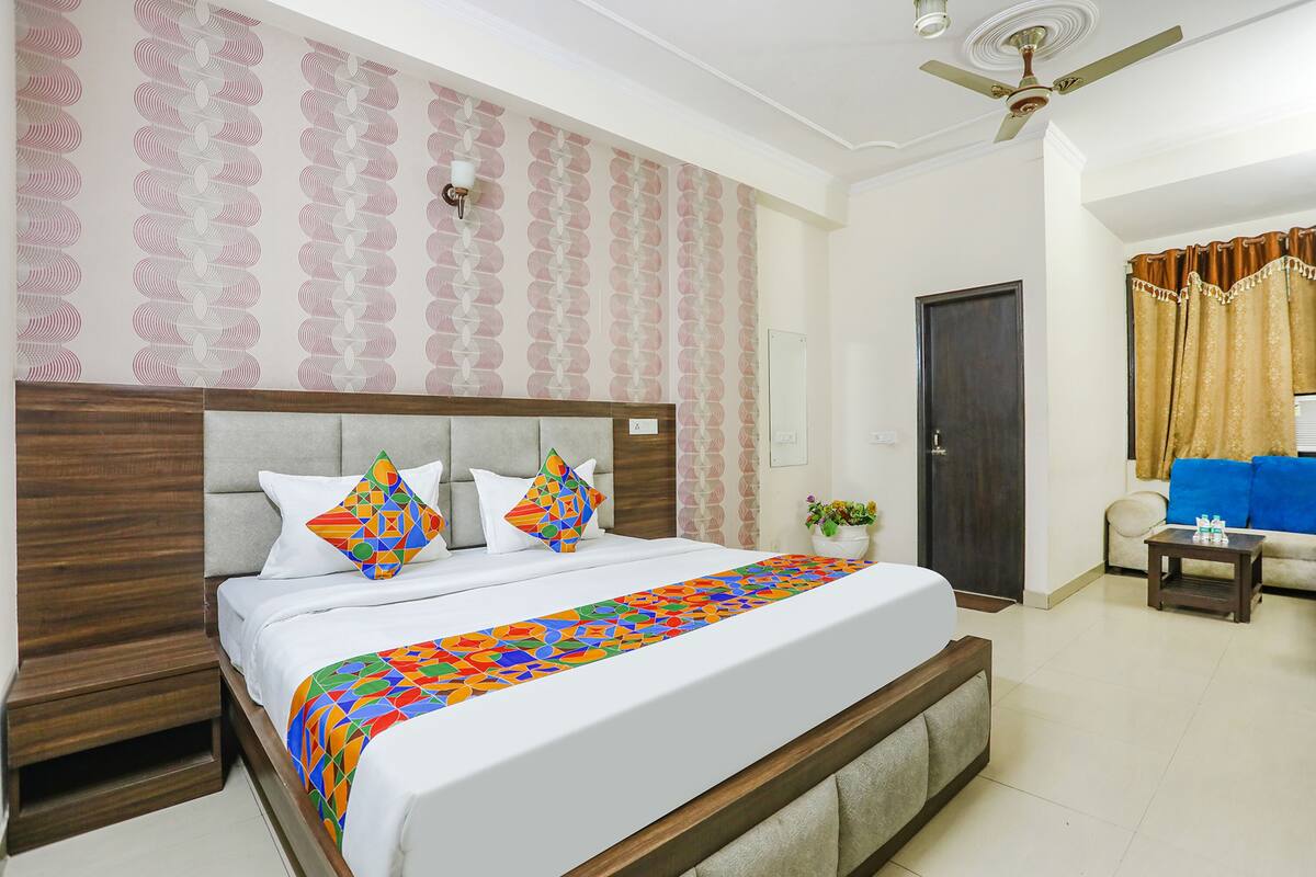 A hotel room with a large bed, a wooden headboard, a ceiling fan, a small table, and a sofa.