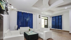 A modern living room with white sofas, a glass coffee table, and blue curtains. - Fabhotel Corporate Stay (Noida)