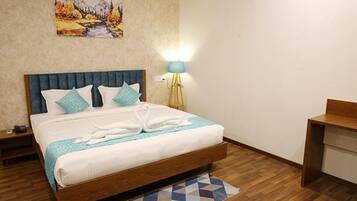 A neatly made bed with a blue headboard, a bedside lamp, and a painting on the wall.