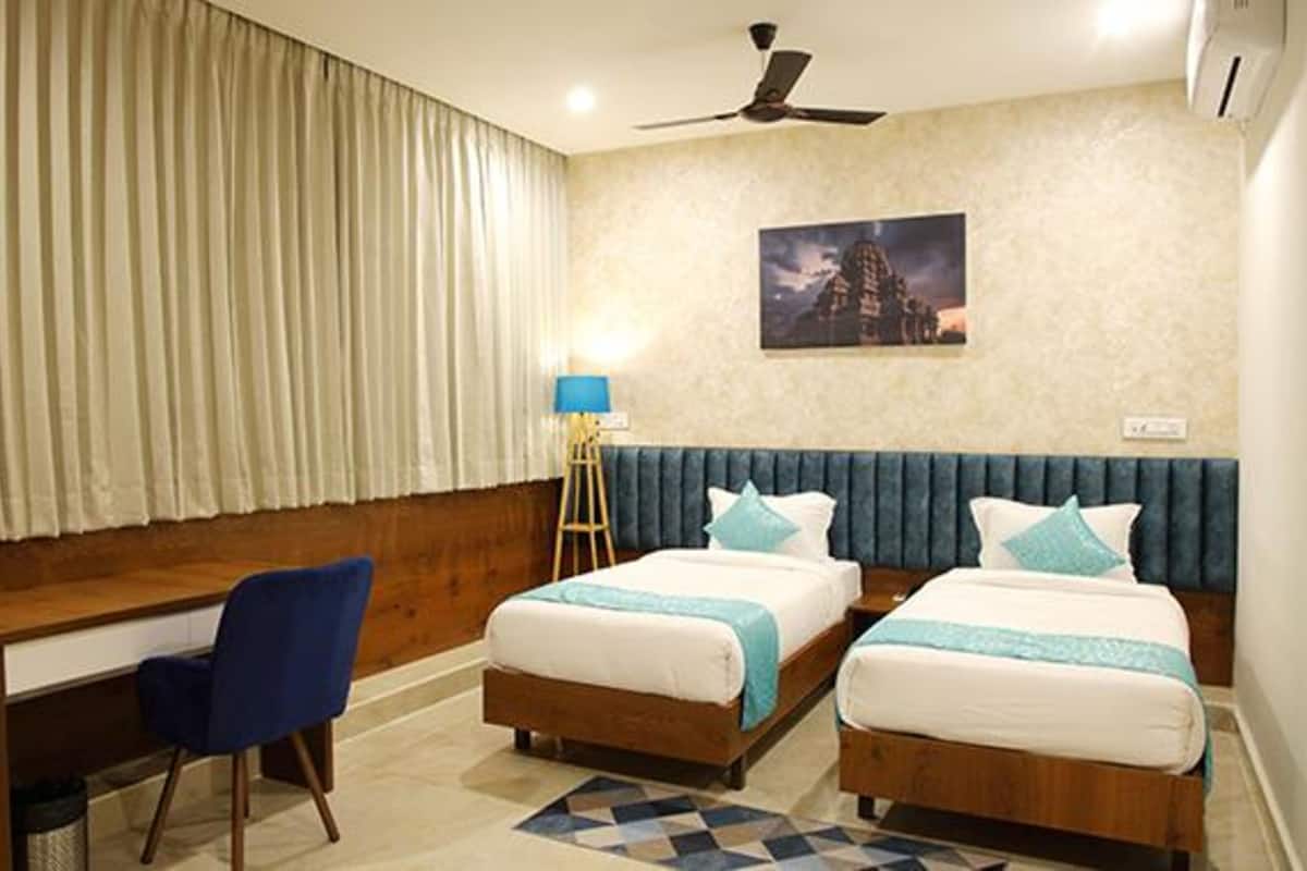 A hotel room with two beds, a desk, a chair, a lamp, and a ceiling fan.