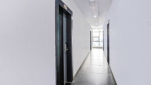A long, narrow hallway with white walls and a black floor. There are doors on both sides, and a light fixture is visible on the ceiling. - Fabhotel Lalitha Elite (Vijayawada)