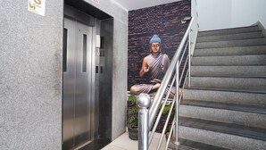 An elevator with a sign indicating the ground floor, a staircase with a metal handrail, and a mural of a seated figure on the wall. - Fabhotel Lalitha Elite (Vijayawada)