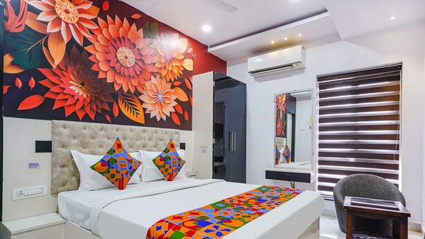 A modern bedroom with a large bed, a colorful geometric throw blanket, a tufted headboard, and a vibrant floral mural on the wall. - Fabhotel Lalitha Elite (Vijayawada)