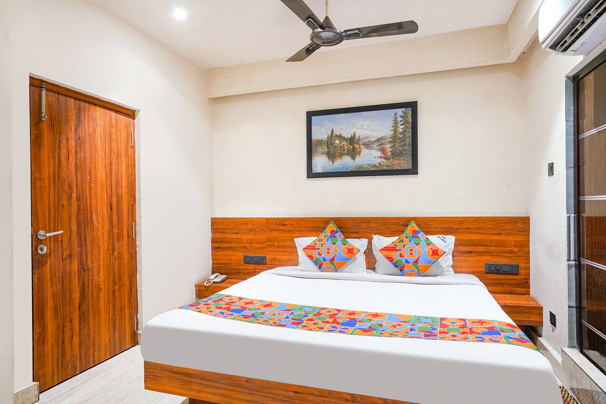 Un dormitorio con cabecera de madera, cama con edredón de diseño geométrico y colores vivos, un cuadro de un lago y un ventilador de techo.