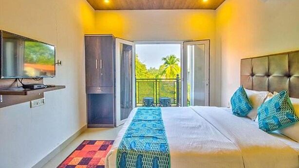 Un dormitorio con cama, televisión, armario y balcón con vistas a zonas verdes.