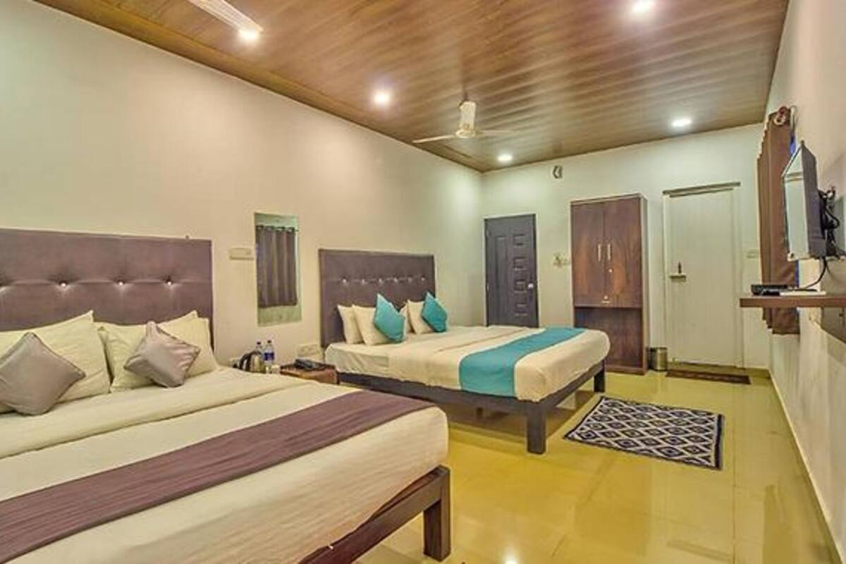 A hotel room with two beds, wooden headboards, a ceiling fan, and a small desk with a chair.