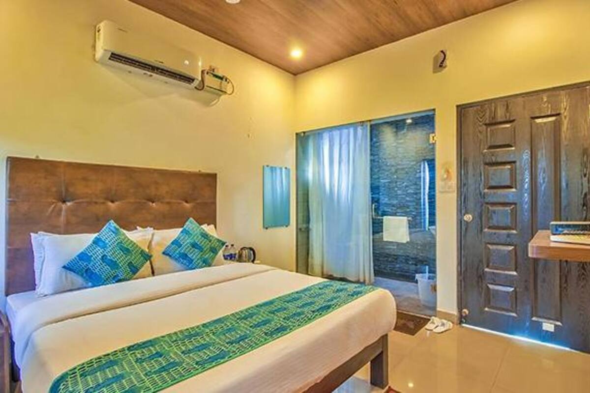 A hotel room with a large bed, a wooden headboard, a desk with a computer, and a view of the sea through a glass door.