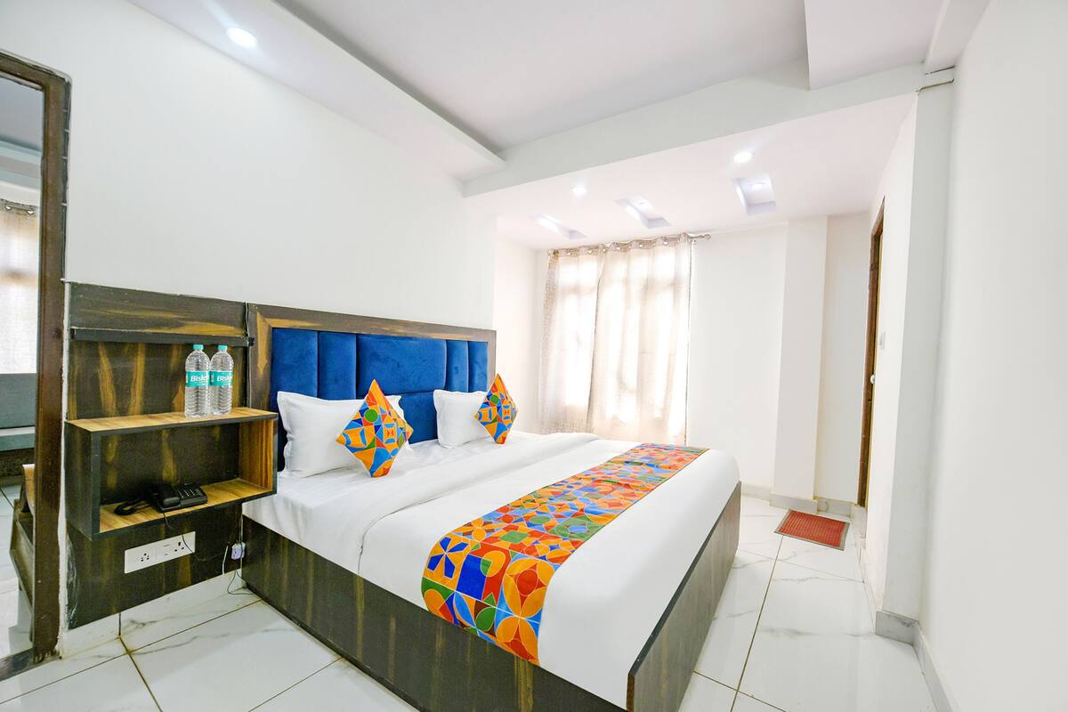 Habitación de hotel con una cama grande, cabecera de madera, mesita de noche con teléfono y ventana con cortinas.