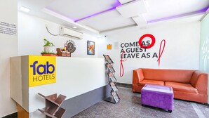 A hotel reception area with a reception desk, a couch, and a purple ottoman. - FabHotel Upstream Sarjapur (Bengaluru)