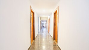 A long, narrow hallway with wooden doors on both sides and a shiny, reflective floor. - FabHotel Upstream Sarjapur (Bengaluru)