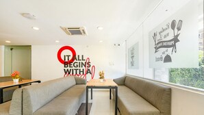 A modern interior with a seating area featuring grey sofas and a wooden table. A wall with motivational text and a window with a view of greenery are visible. - FabHotel Upstream Sarjapur (Bengaluru)