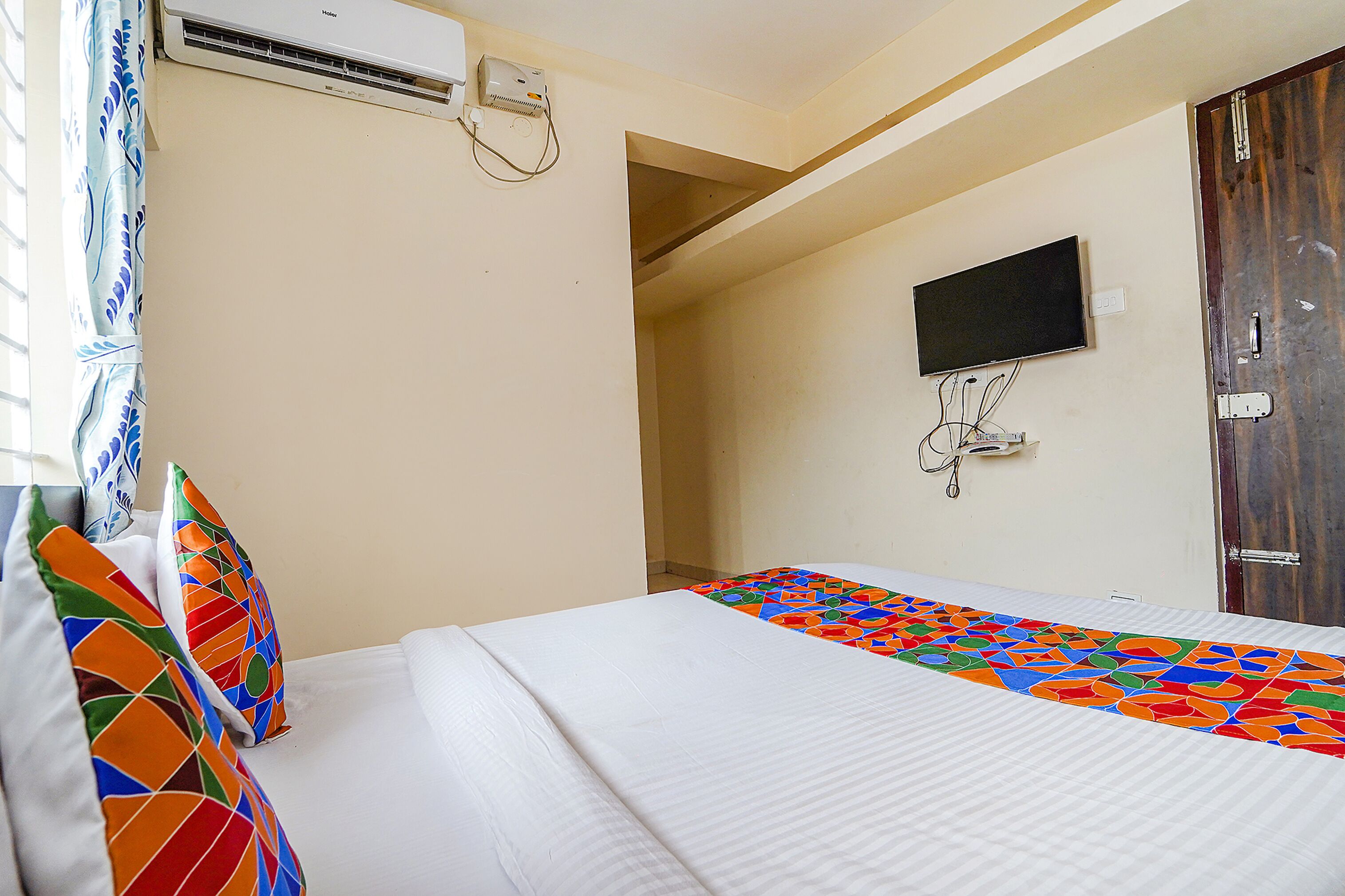 A hotel room with a bed, a television mounted on the wall, and an air conditioning unit.