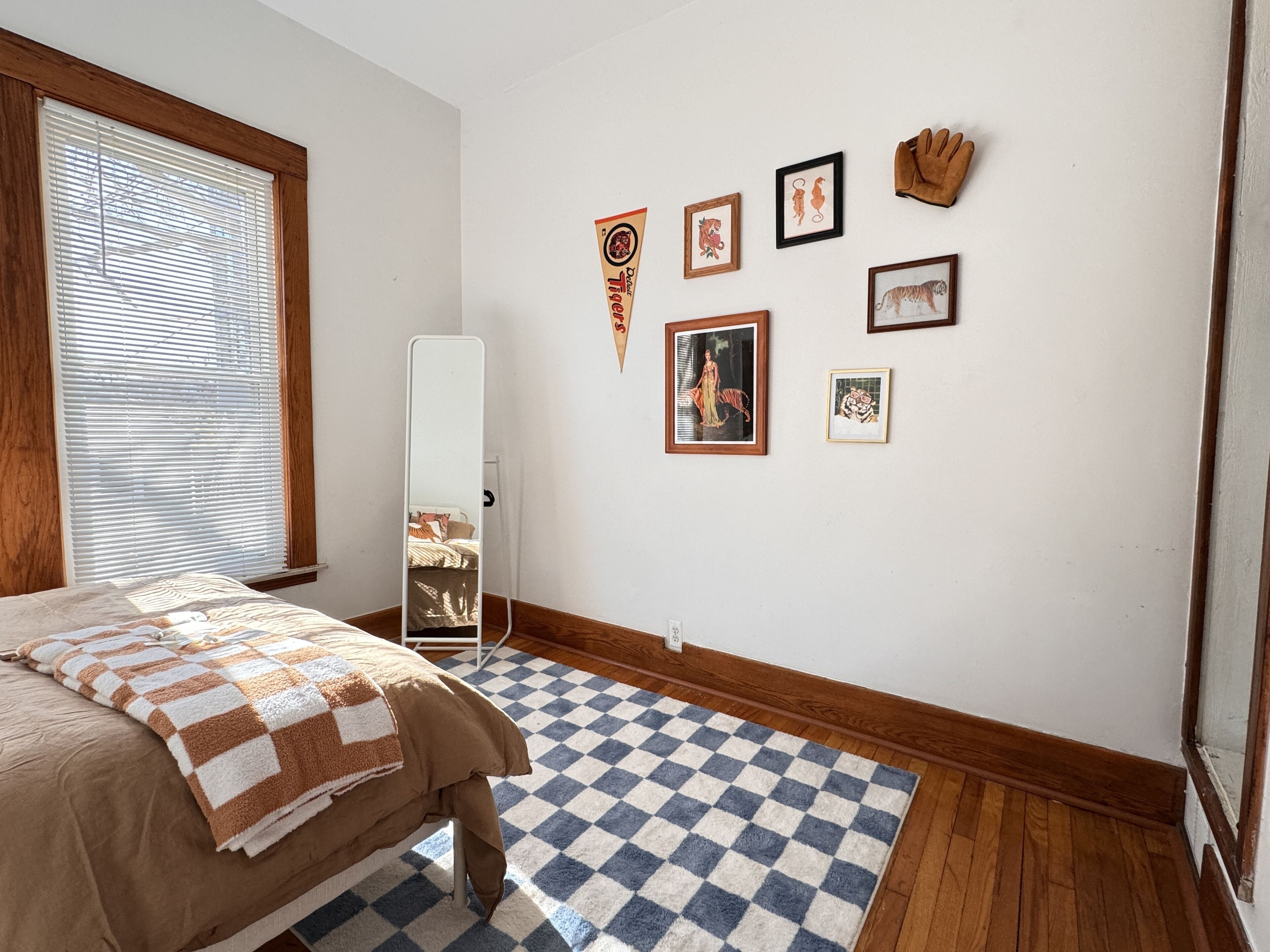 Quarto com cama, tapete xadrez, espelho e várias quadros na parede.