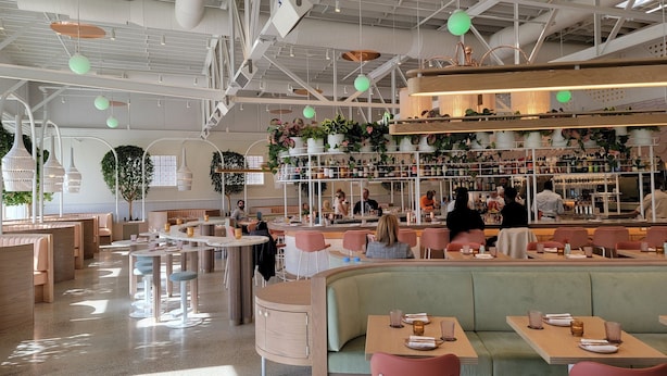 Un restaurante moderno con techos altos, conductos expuestos y diferentes opciones de asientos, incluyendo cabinas y mesas.
