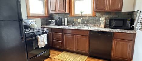 A kitchen with wooden cabinets, a black refrigerator, a stove, a microwave, and a sink.
