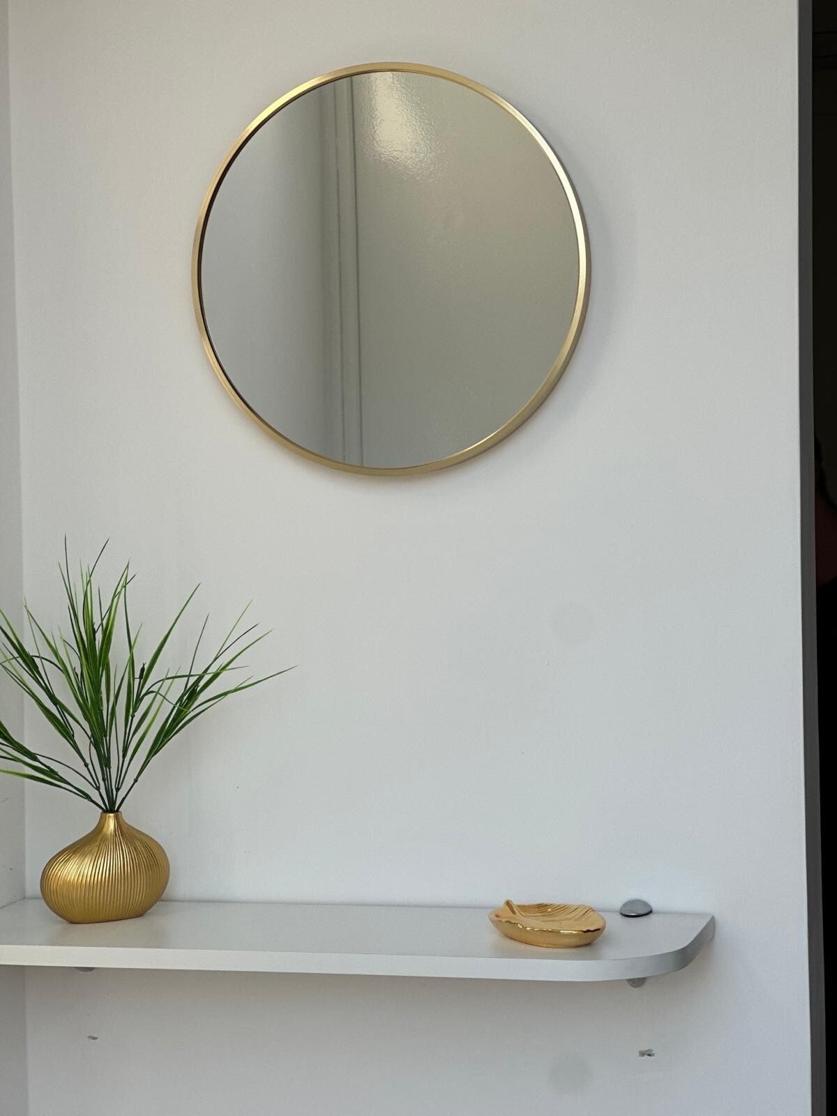 A white wall with a round mirror and a shelf below it.