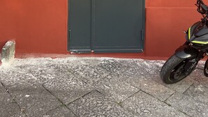 Une porte fermée, de couleur sombre, avec une poignée en métal, une petite enseigne portant un logo, et une moto garée à côté.