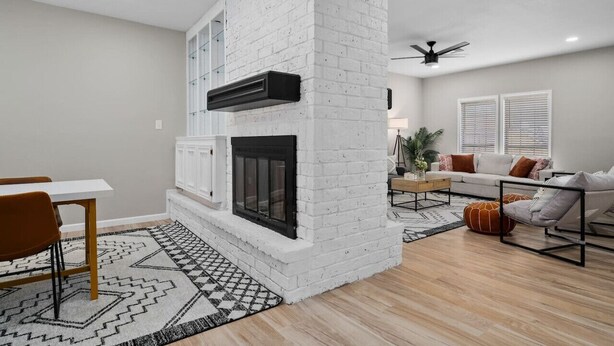 Una sala moderna con chimenea de ladrillo blanco, un comedor con mesa y sillas, y una zona de estar con sofá y cojines.