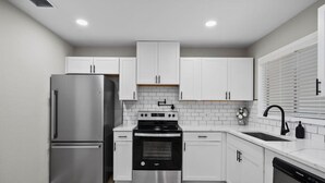 Una cocina moderna con armarios blancos, electrodomésticos de acero inoxidable y un salpicadero de azulejos.
