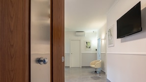 A hallway with a wooden door, a modern chair, a flat-screen TV, and a framed artwork on the wall. - Rua de Mar Portici (Portici)