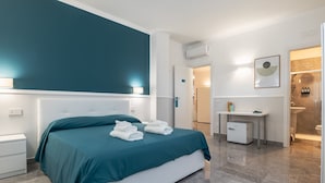 A modern hotel room with a large bed, a bedside table, a desk, and a bathroom visible through an open door. - Rua de Mar Portici (Portici)