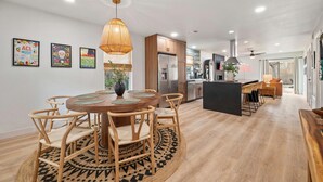 A modern kitchen with wooden cabinets, a central island, and a dining area with a round table and chairs. - Barton Hills Hideaway + Hot Tub - Magdalena 1! (Austin)