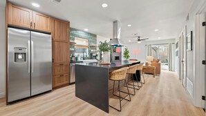 A modern kitchen with stainless steel appliances, wooden cabinets, and a central island with bar stools. - Barton Hills Hideaway + Hot Tub - Magdalena 1! (Austin)