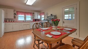 A dining room with a wooden table set for four, surrounded by white cabinets and a kitchen in the background. - Walter & Mae's Farmhouse: Charming accomodations with gorgeous mountain views (Elizabethton)